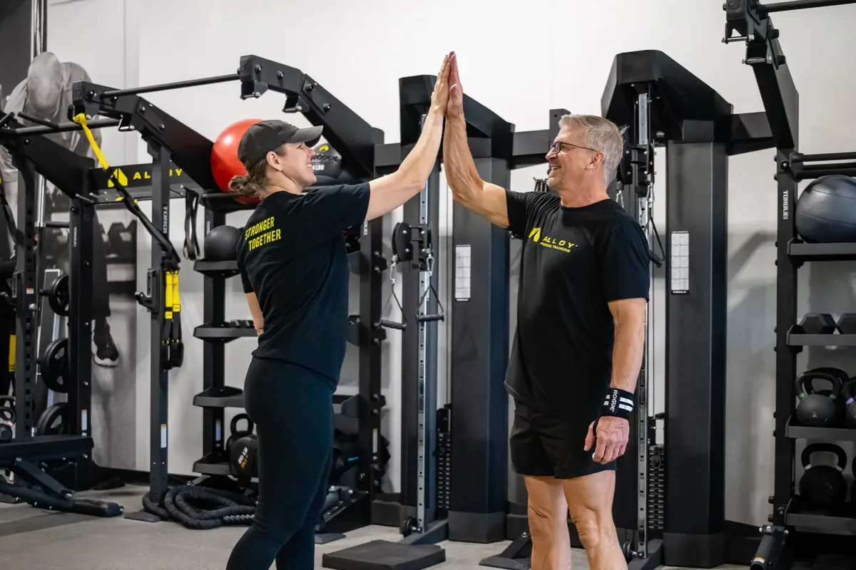 Two members share a high-five between racks on the training floor of an Alloy studio