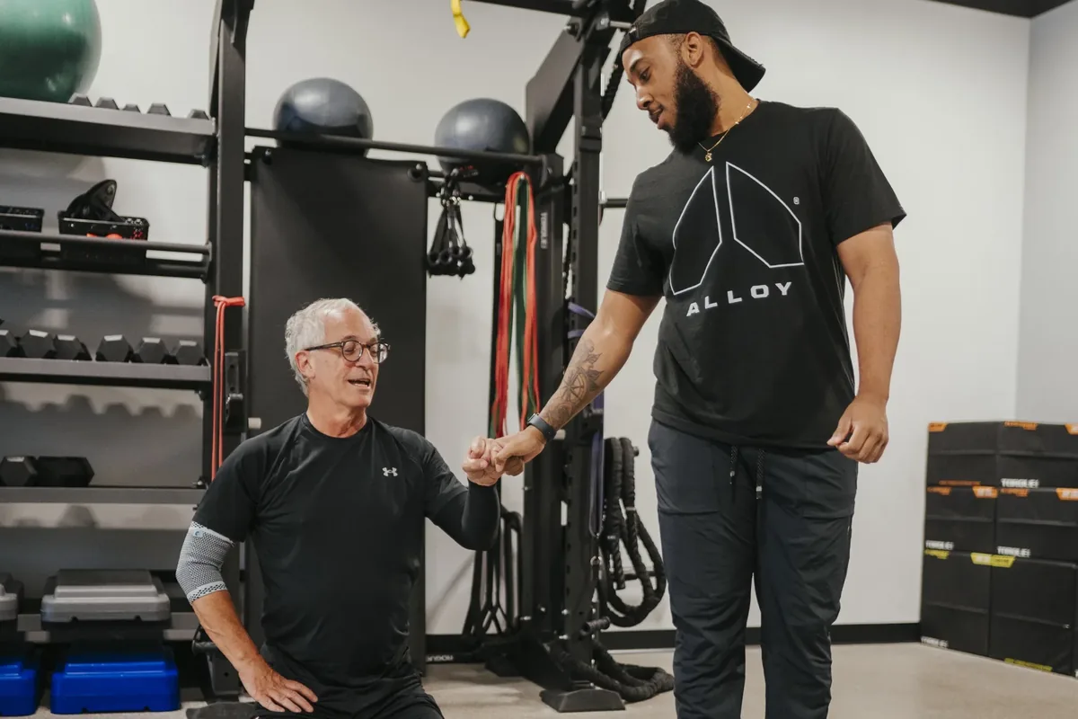 A coach encourages an older member as he works through a set at an Alloy Personal Training studio