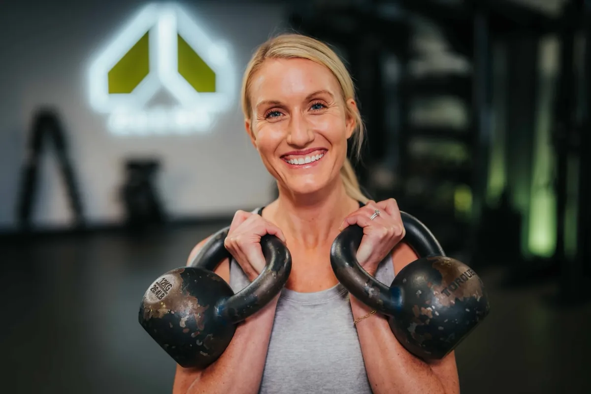 A member holds two kettlebells racked at her shoulders during a strength session at an Alloy studio