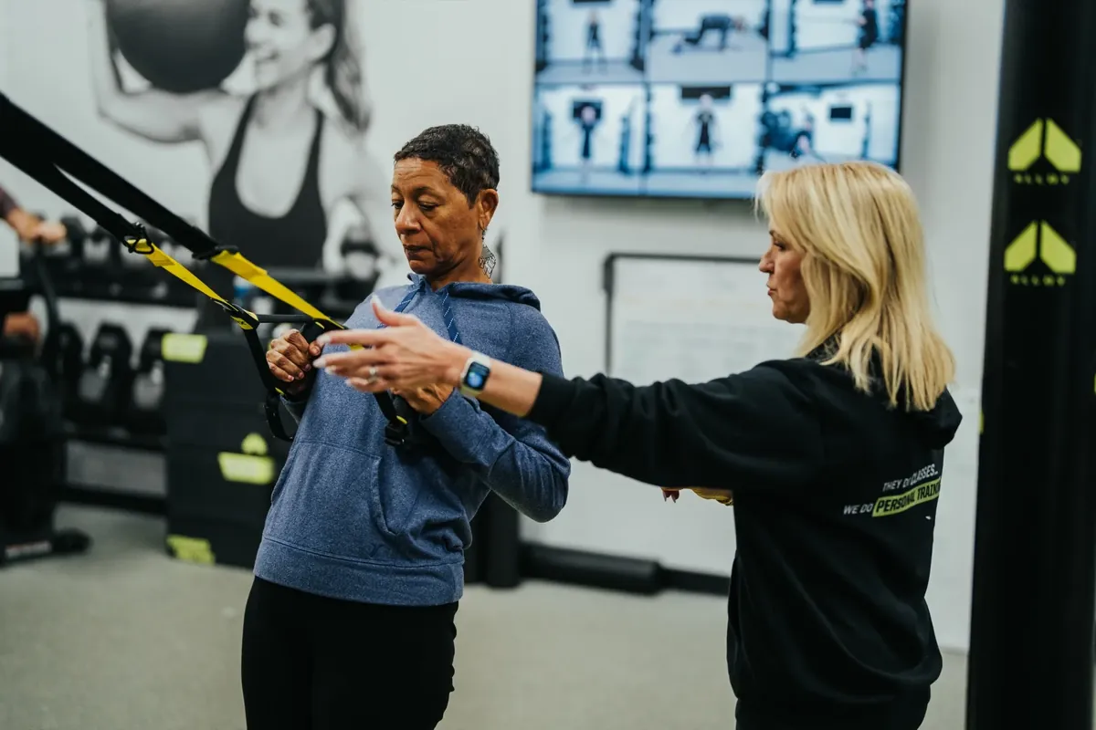 An Alloy coach positions a member's arms during a TRX exercise
