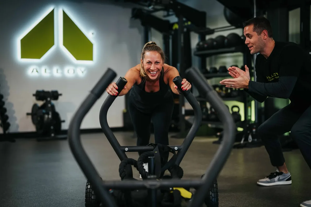 An Alloy coach cheers on a member pushing a training sled